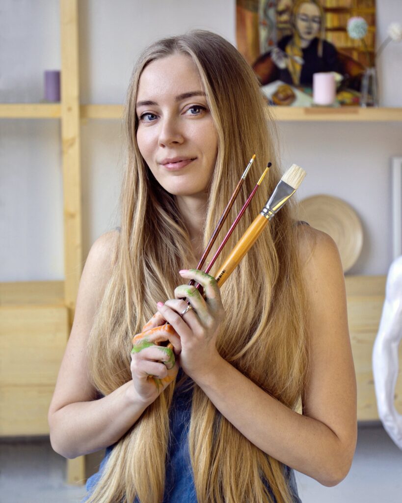 Lana Swan holding paintbrushes in her studio, portrait from the AL-TIBA9 Magazine interview