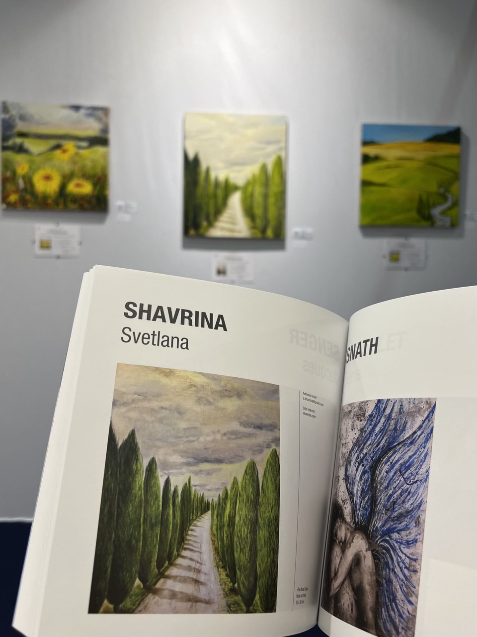 Page about Svetlana Shavrina in the art3f Mulhouse 2024 catalogue, with her landscape paintings exhibited behind