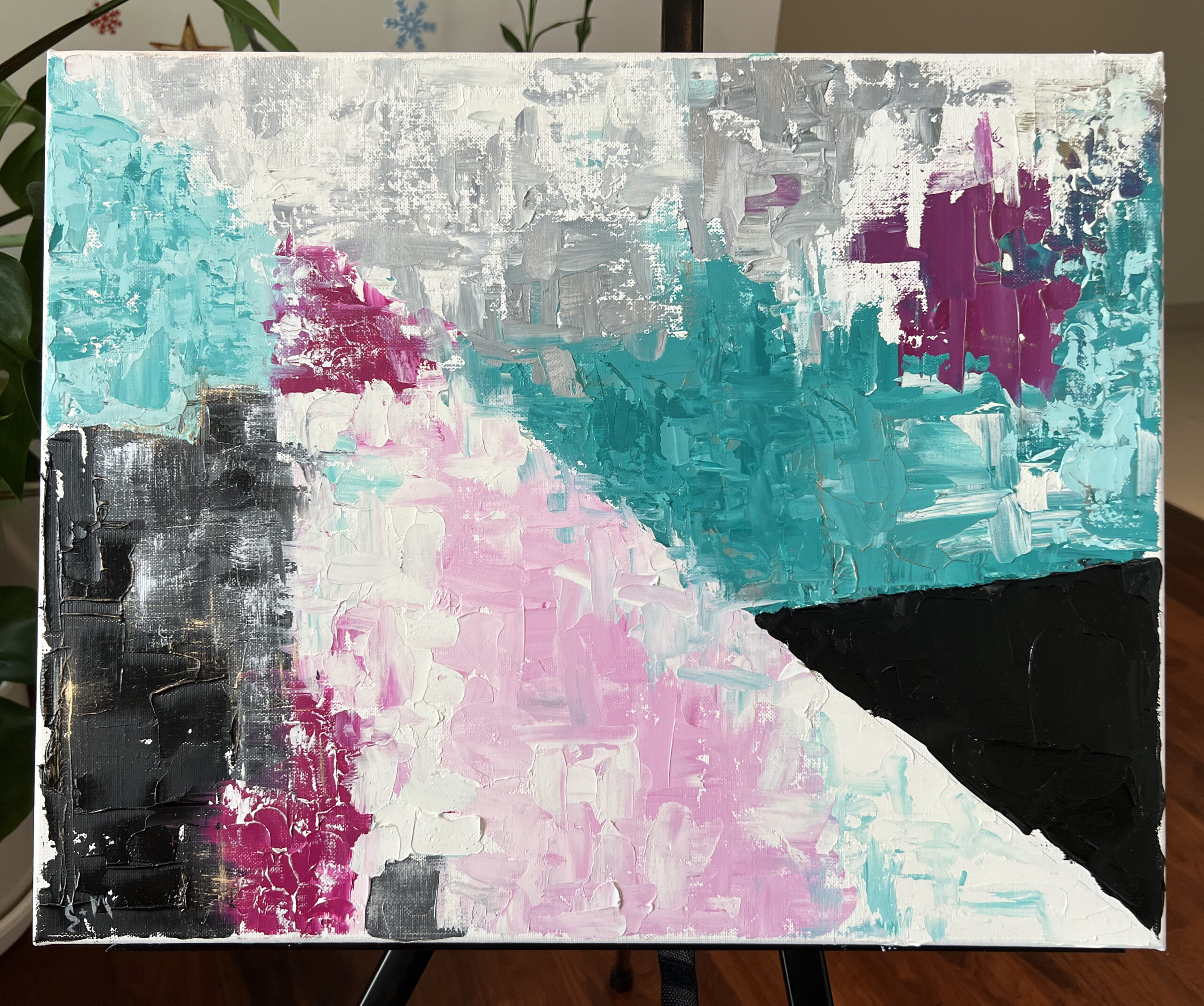 Black Triangle oil painting by Lana Swan on a black easel beside green house plants