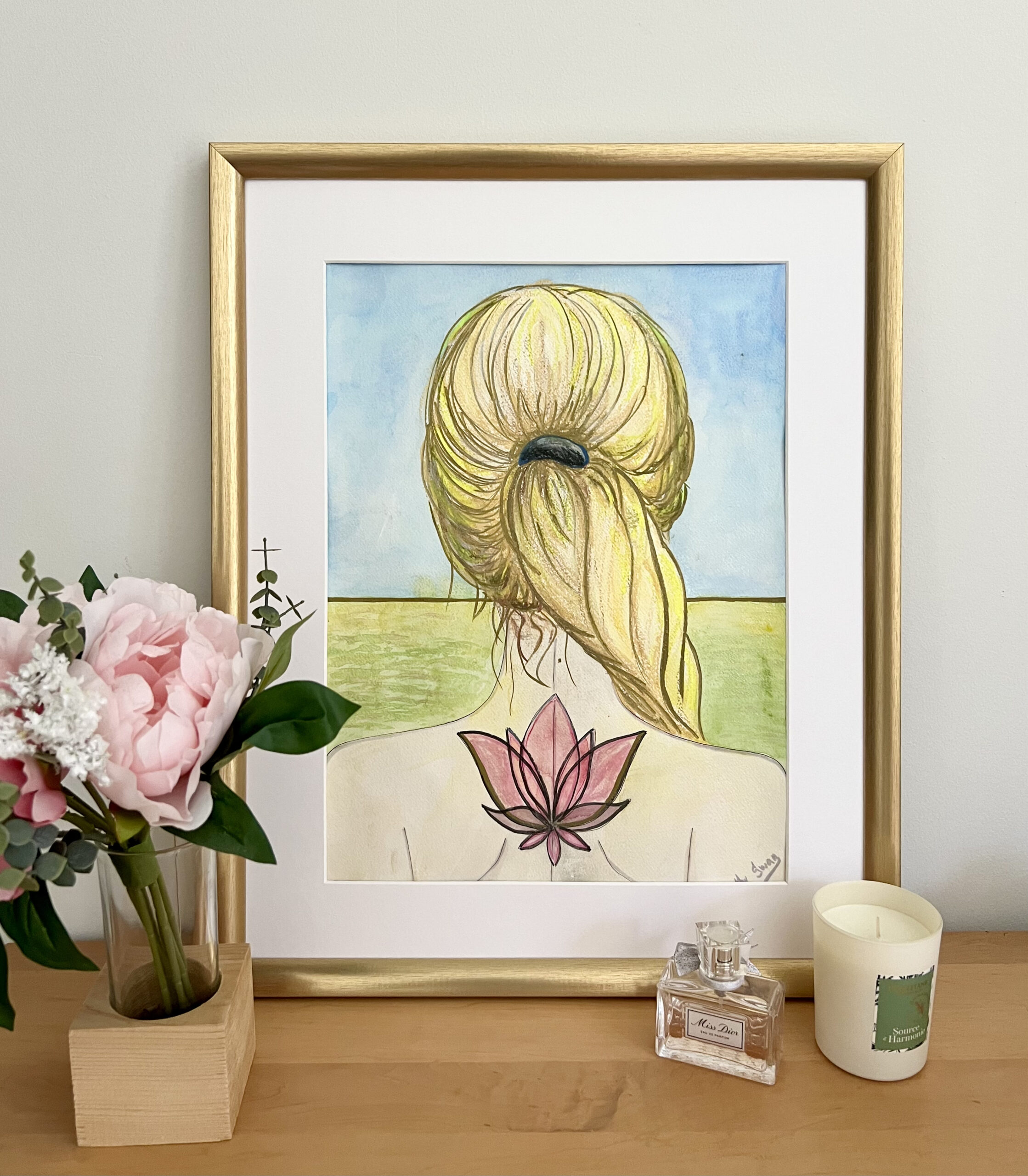 New Reality by Lana Swan in a gold frame on a sideboard beside pink peonies and a candle